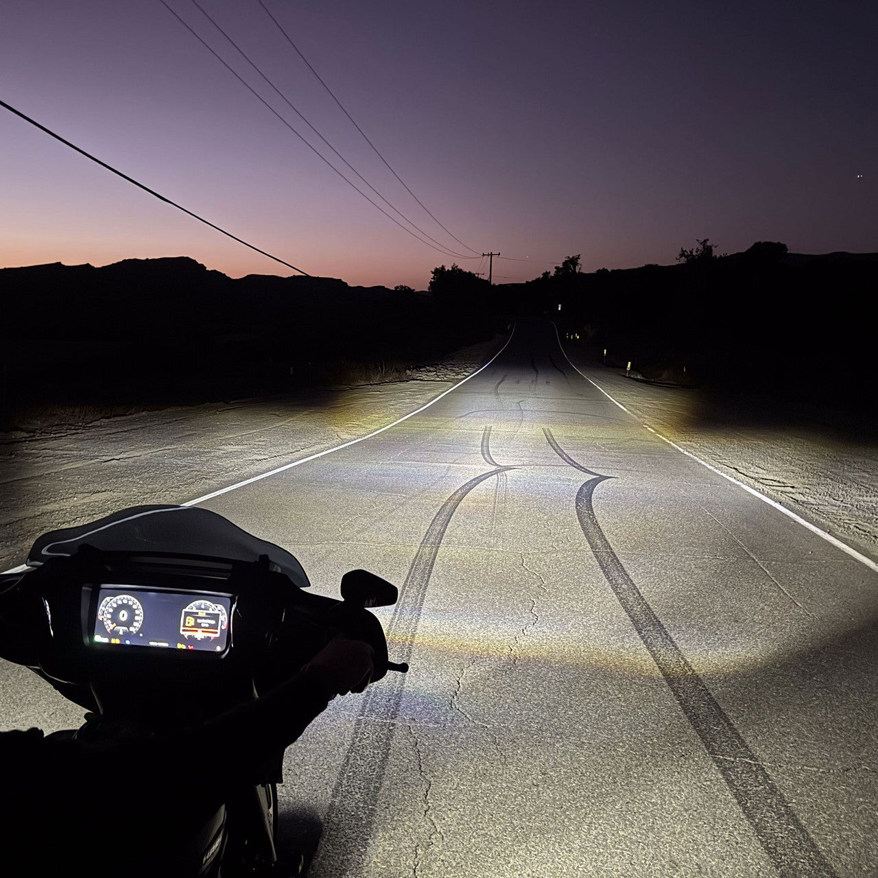 Motorcycle on a dark road with headlights illuminating the path